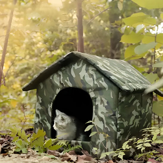 Niche pour chat extérieur camouflage avec chat blanc regardant dehors, installée dans un jardin forestier ensoleillé