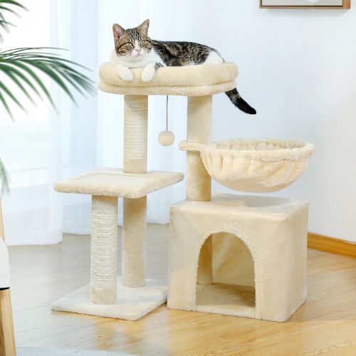 Chat tigré endormi sur le plateau supérieur d’un arbre a chat beige avec hamac et niche, griffoirs en sisal posés dans un salon lumineux.
