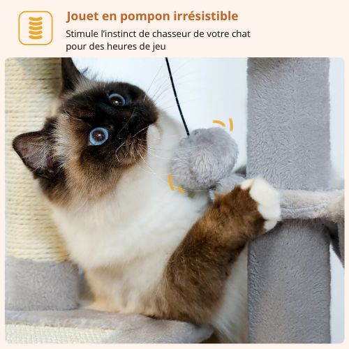 Chat jouant avec un jouet pompon suspendu sur un arbre à chat en peluche, griffoir en sisal et poteau rembourré pour stimuler son instinct de chasseur.