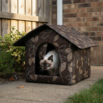 Niche pour chat extérieur en tissu motif feuilles avec chat siamois observant de l'entrée ouverte, installée dans un allée de jardin.